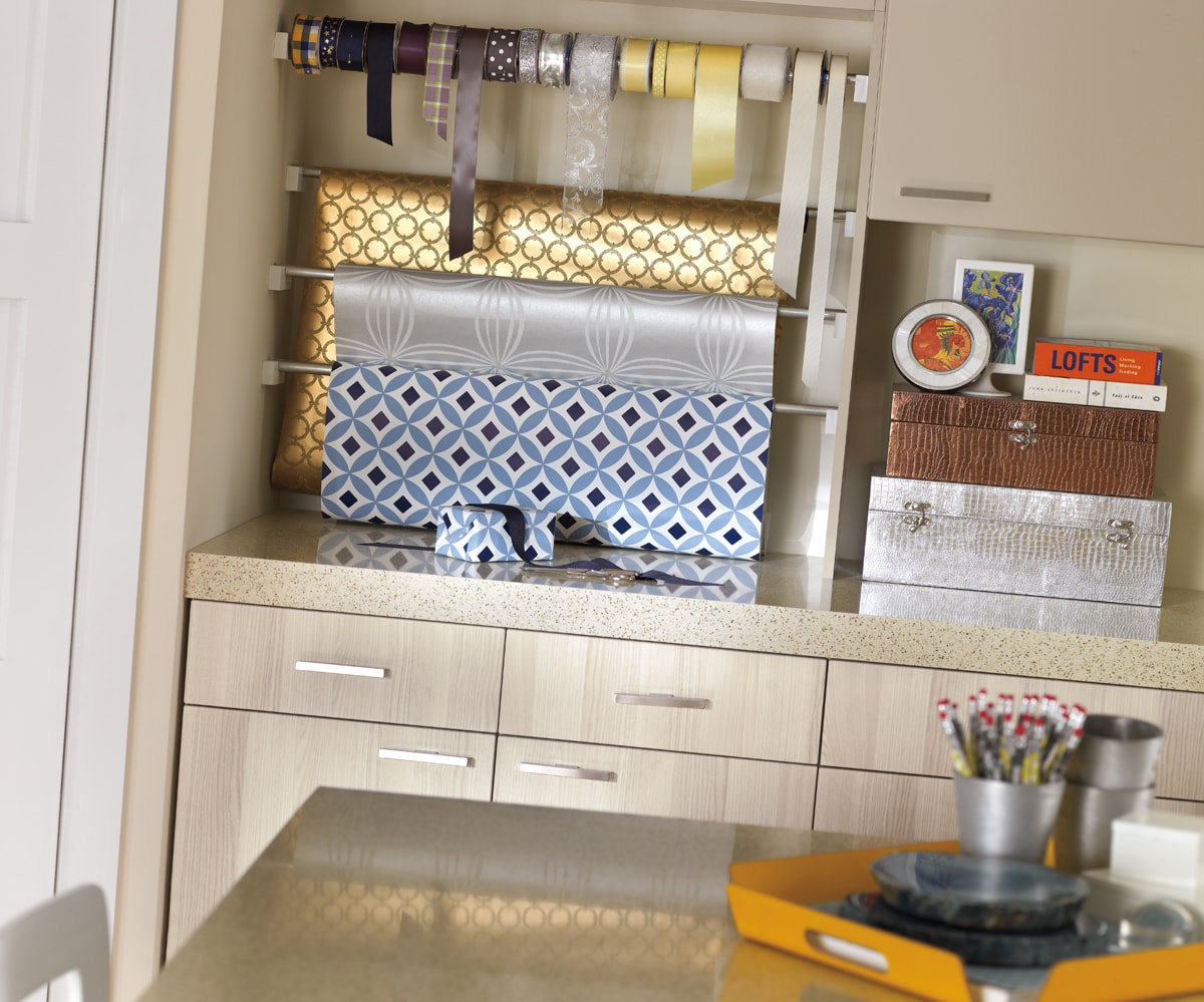 Beige cabinets with hanging wrapping paper and ribbons on dowels.