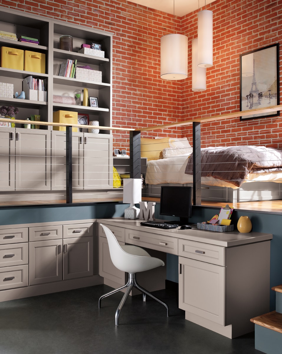 Grey corner desk in a modern brick bedroom with built-in grey cabinets.