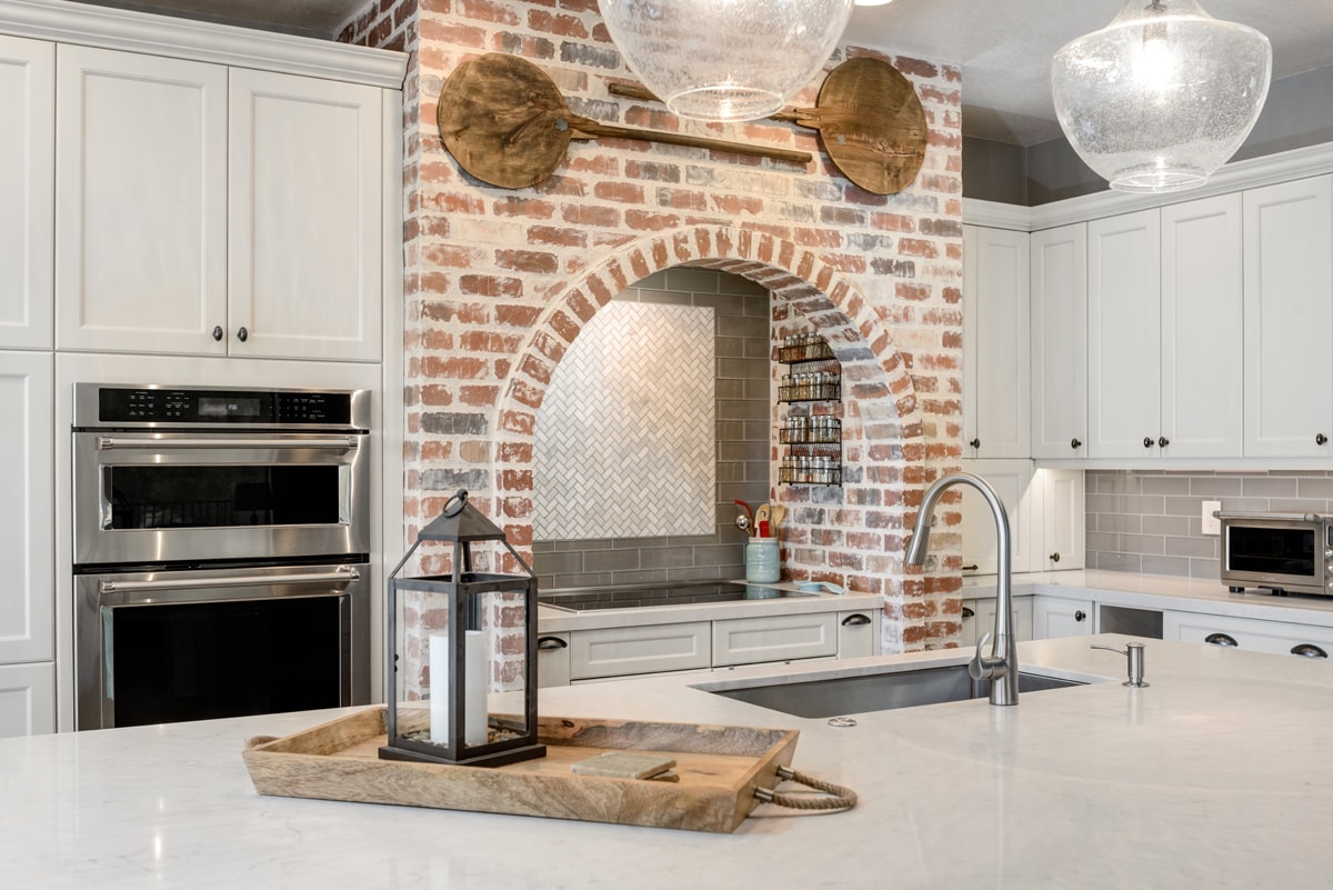 A large brick arch is acting as the focal point in a kitchen with white cabinets.