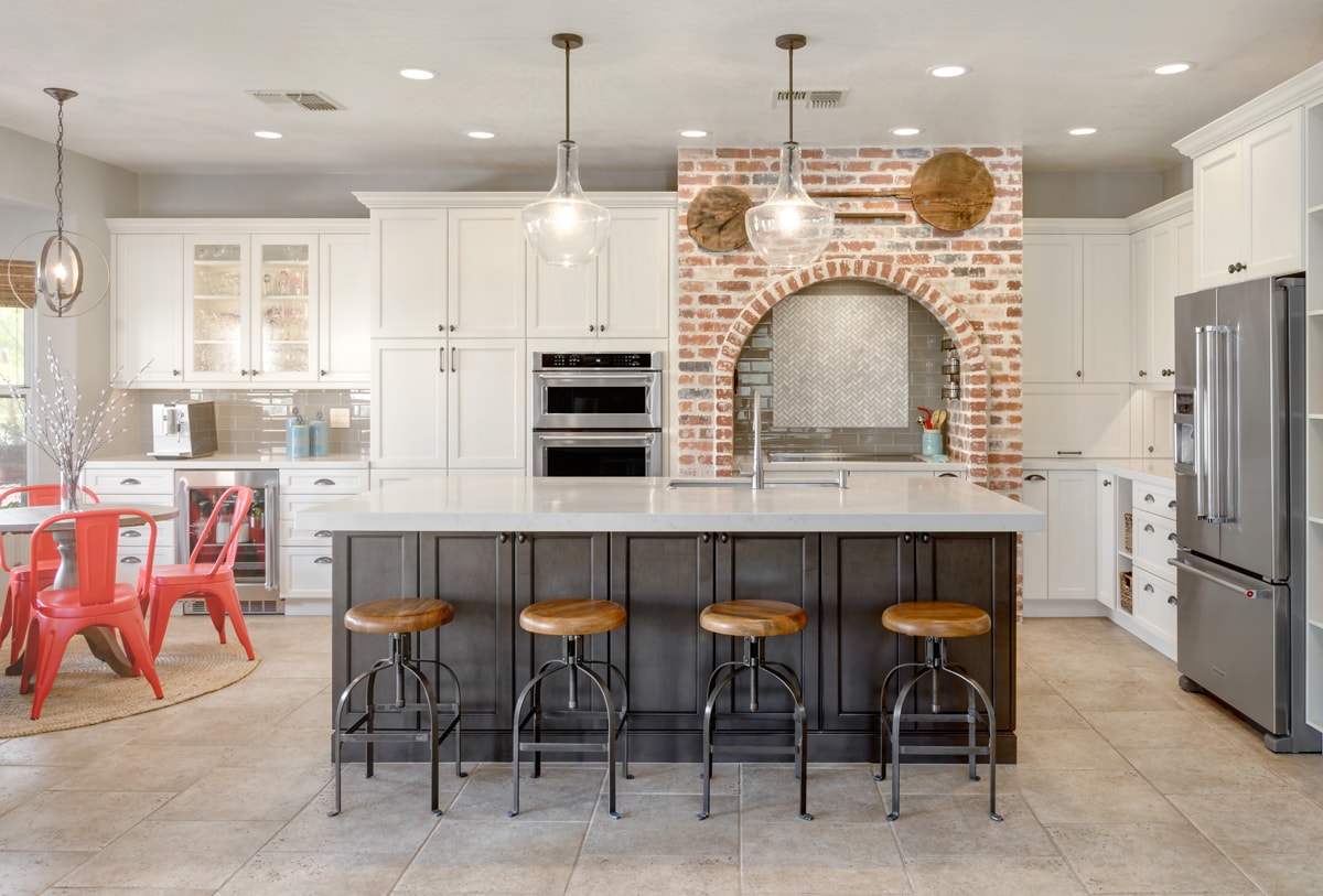 A Transitional style kitchen witha large brick arch and orange dining chairs.