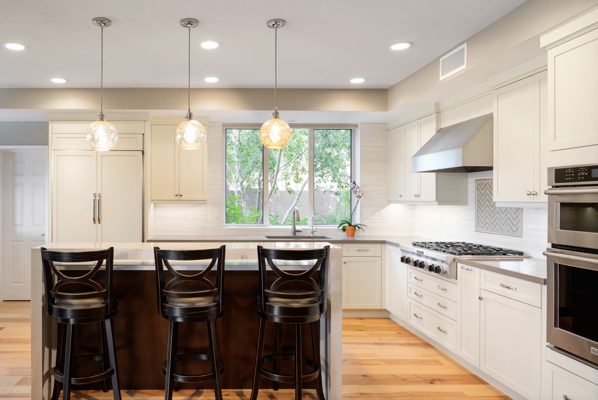 Wide shot of a kitchen with tall white cabinets and a dark brown island with bar seating.