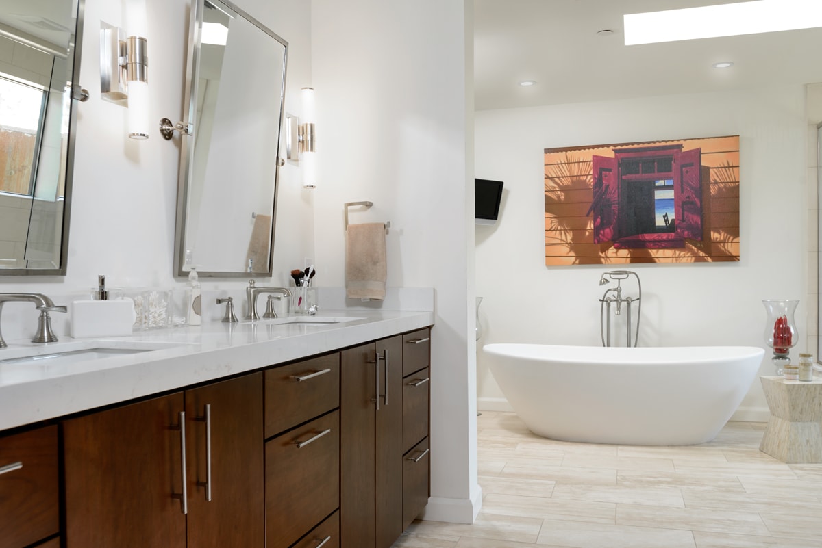 A warm wood vanity with slab-style cabinets with a white freestanding bathtub in the background.