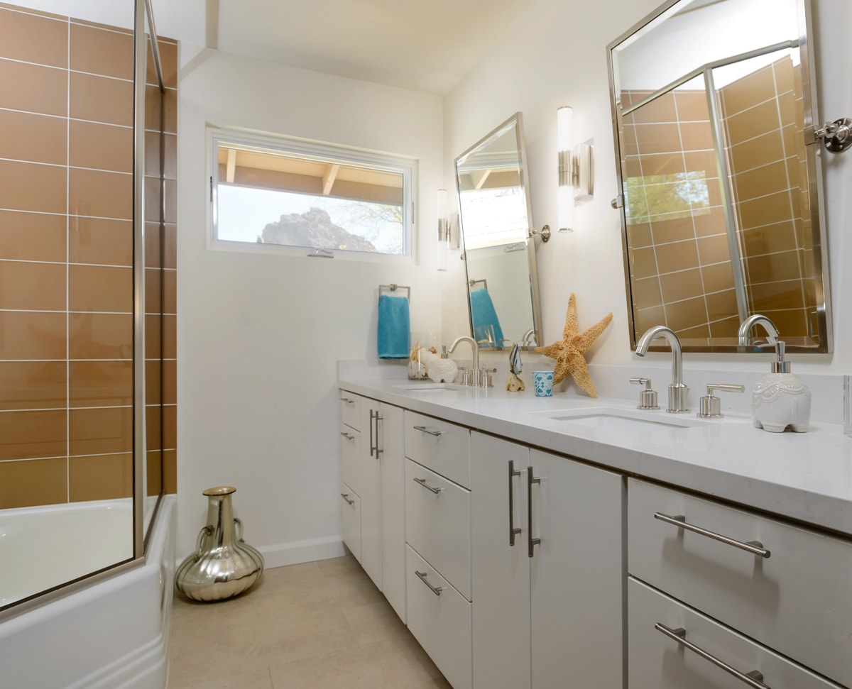 A white bathroom vanity with a starfish accessory and sand colored shower tile