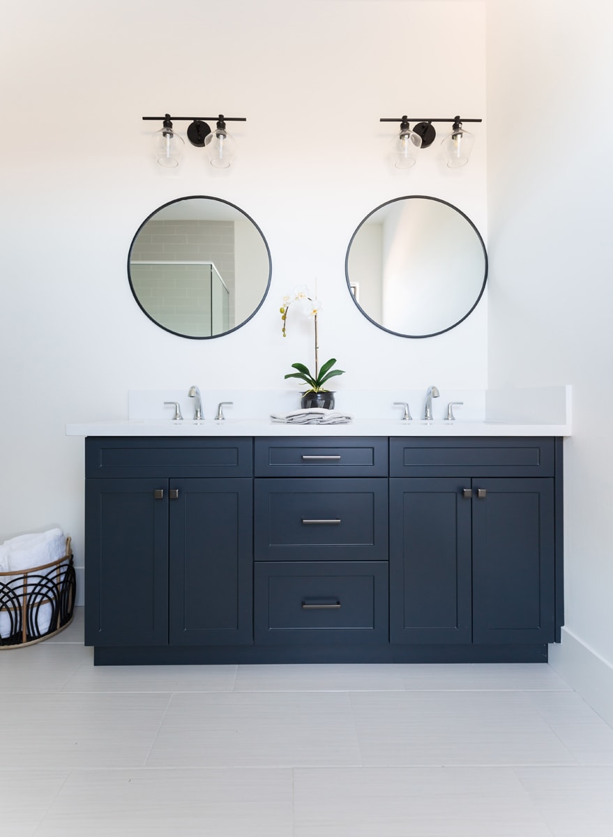 A navy blue double vanity with black hardware in a bathroom with white walls and white flooring.