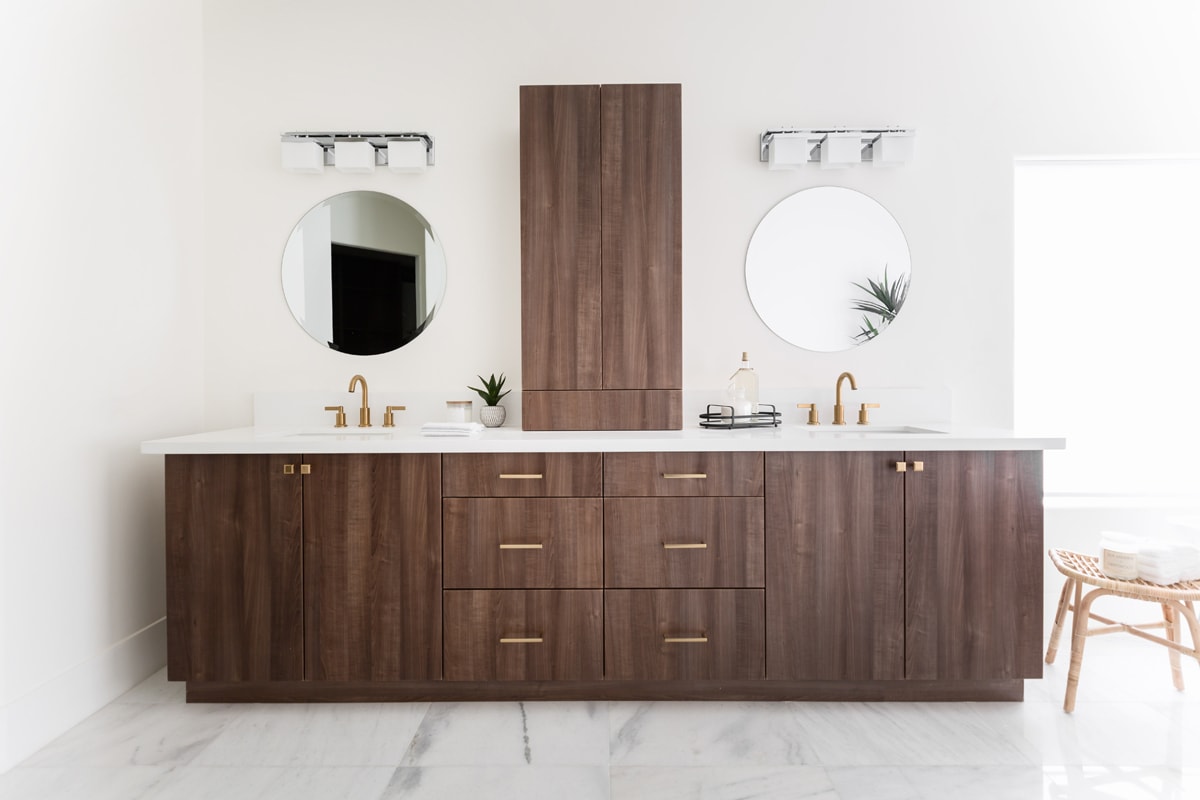 A Contemporary double vanity with slab-style brown cabinetry with a round mirror on top of each sink.