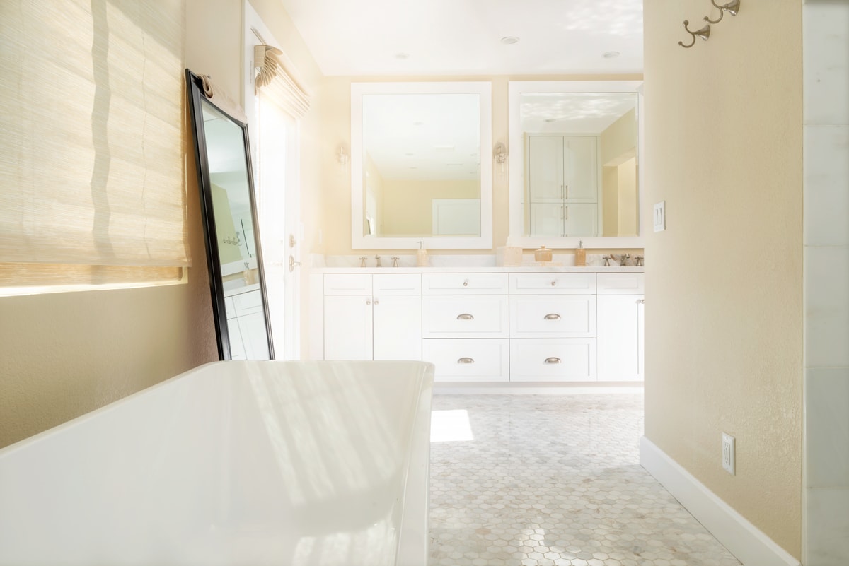 A white bathtub in the foreground with a long white double vanity in the background.