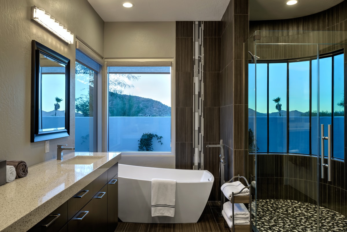 Bathroom with a long dark brown vanity, a freestanding white bathtub and a large glass shower.