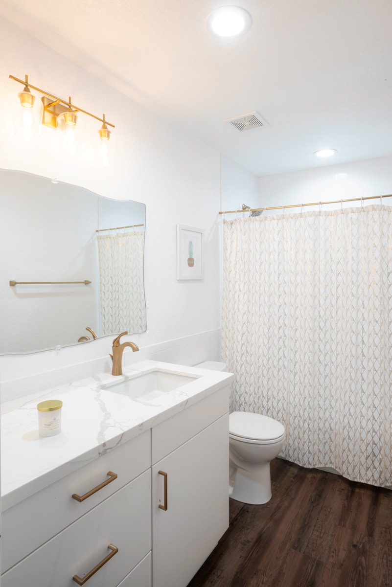 White vanity and countertop with gold hardware and light fixtures.