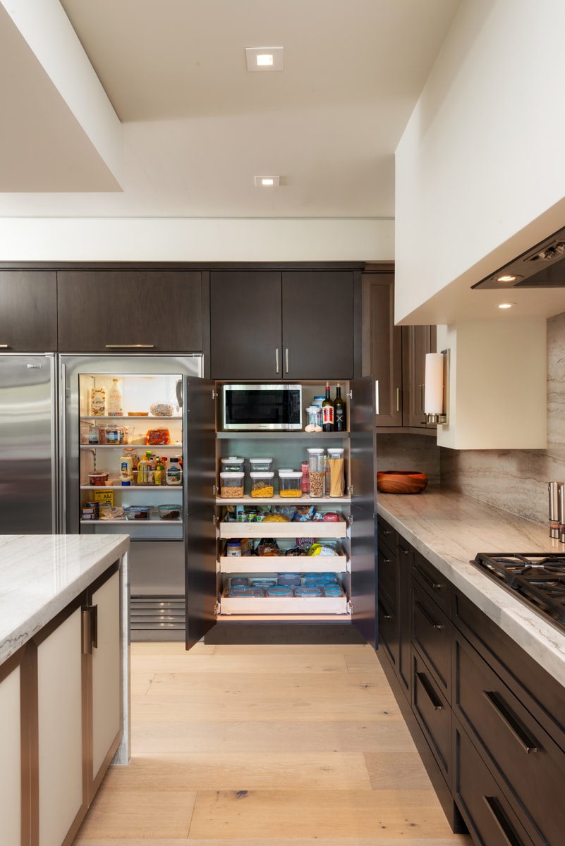 Tall dark brown pantry beside large stainless fridge.