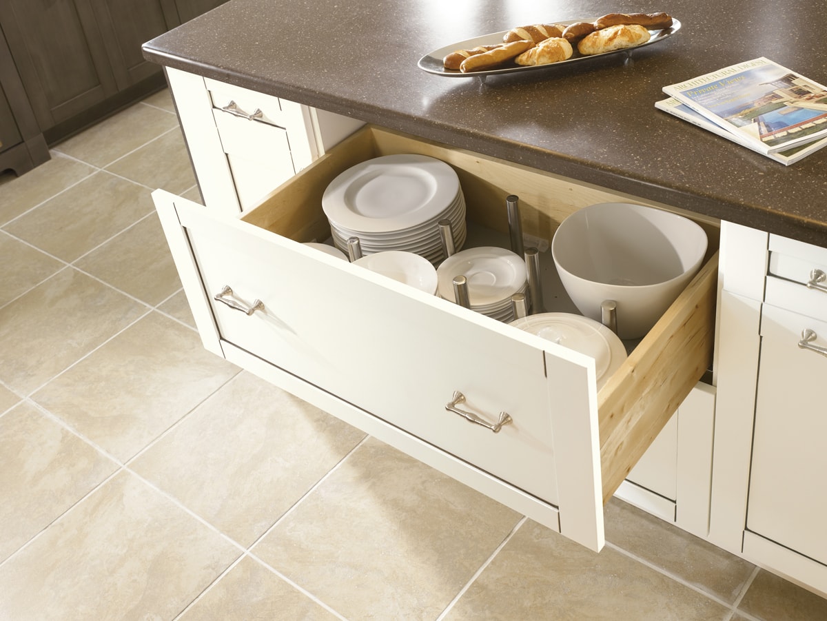 Open white cabinet drawer with dishes and peg organizers.