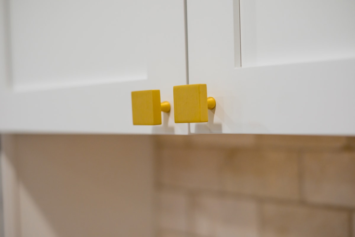 Close up of a white kitchen cabinet with bright yellow square hardware pulls.