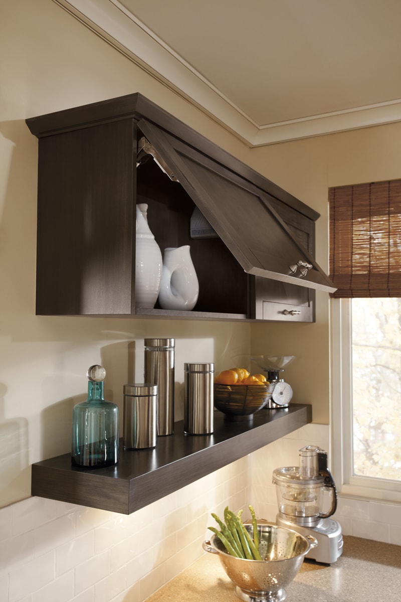 Dark brown lift-up cabinetry with one long floating shelf displaying accessories underneath.