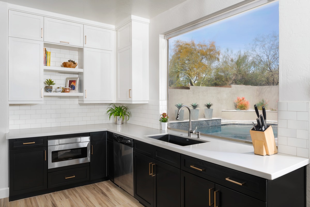A kitchen with white upper cabinetry and black lower cabinetry with a white subway tile backsplash.