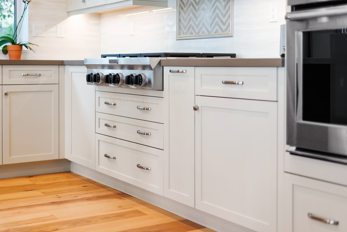 Lower white shaker style kitchen cabinets with distressed wood flooring.