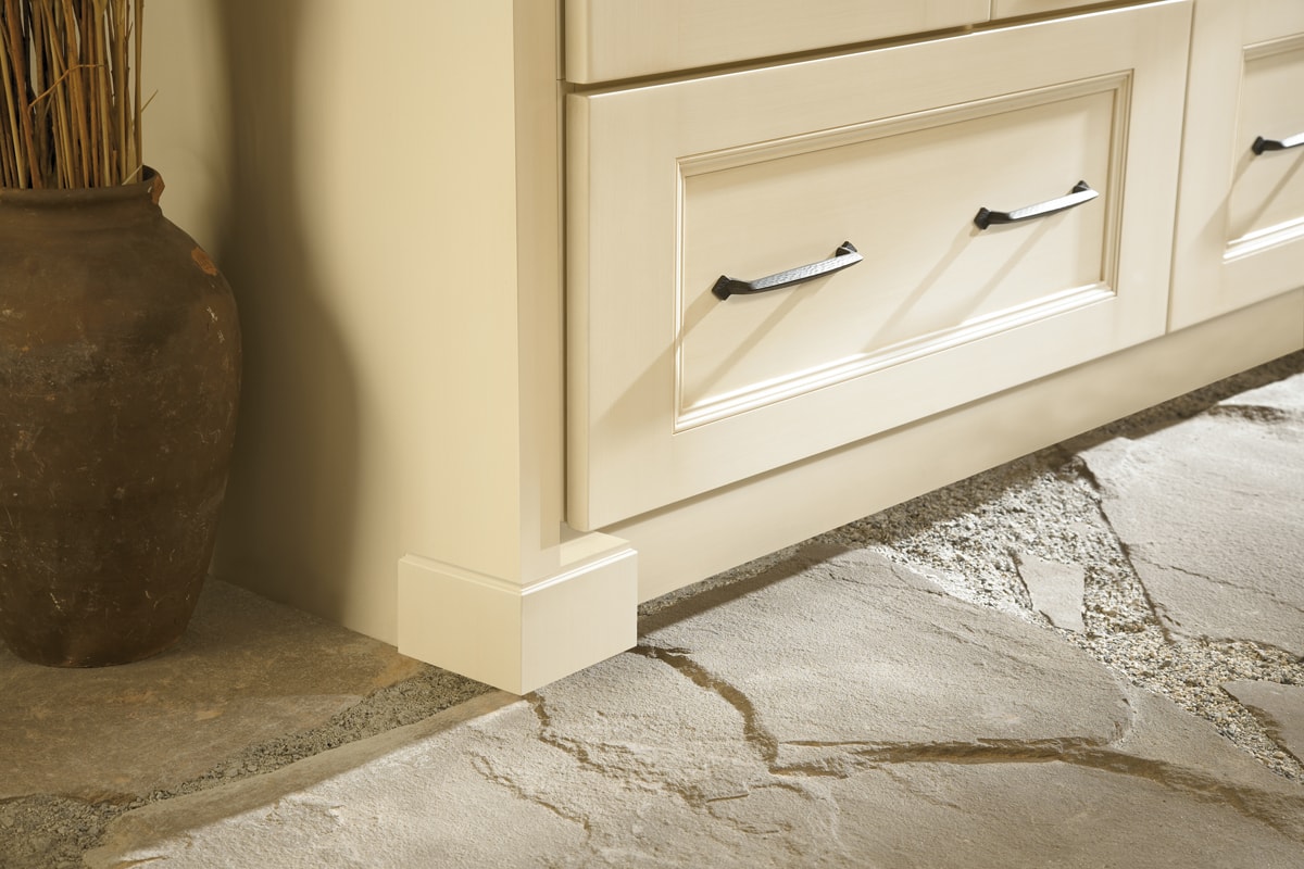 Bottom corner of a cream cabinet beside beige tile flooring.