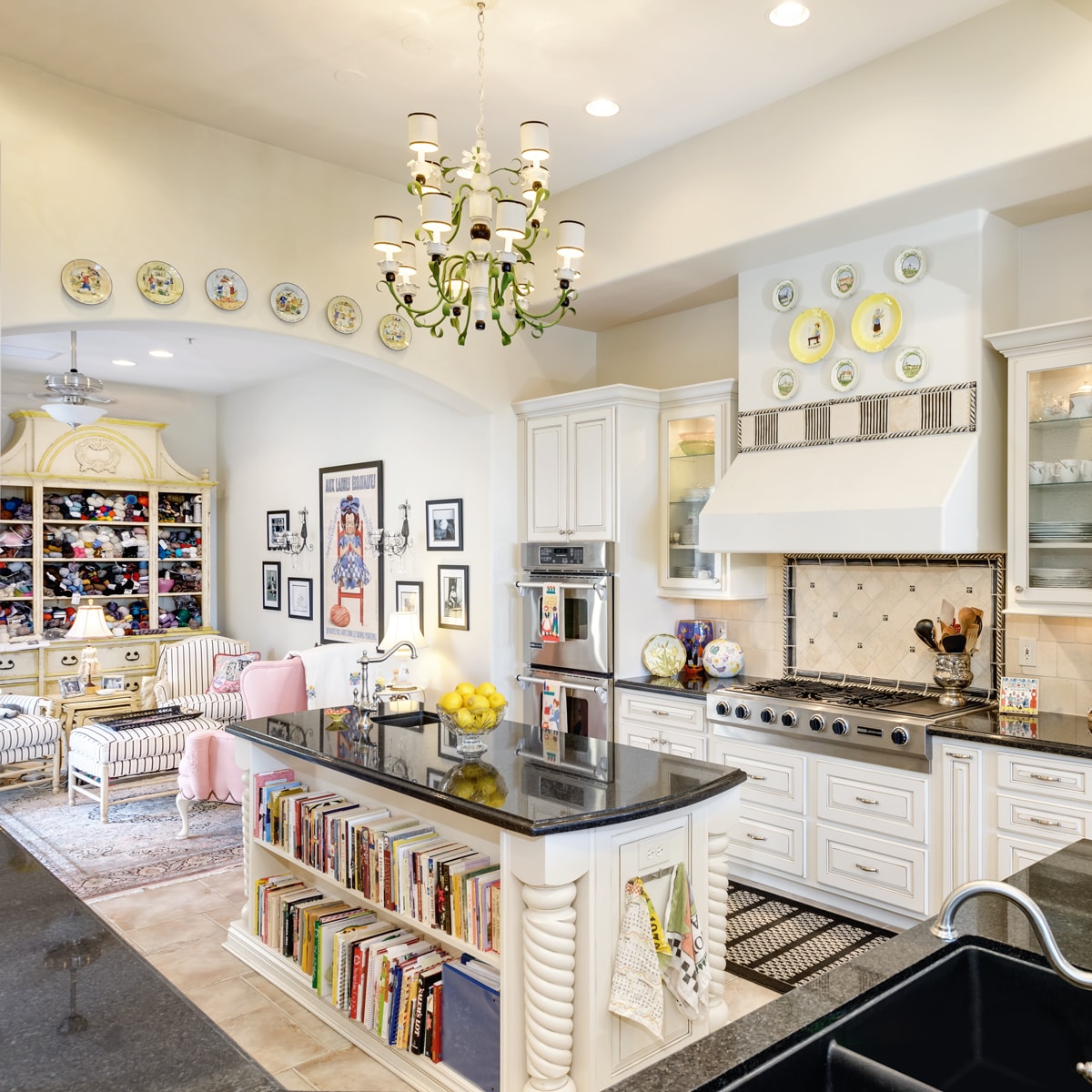 A Traditional designed kitchen with decorative plates, a large chandelier and a kitchen island with a bookshelf.