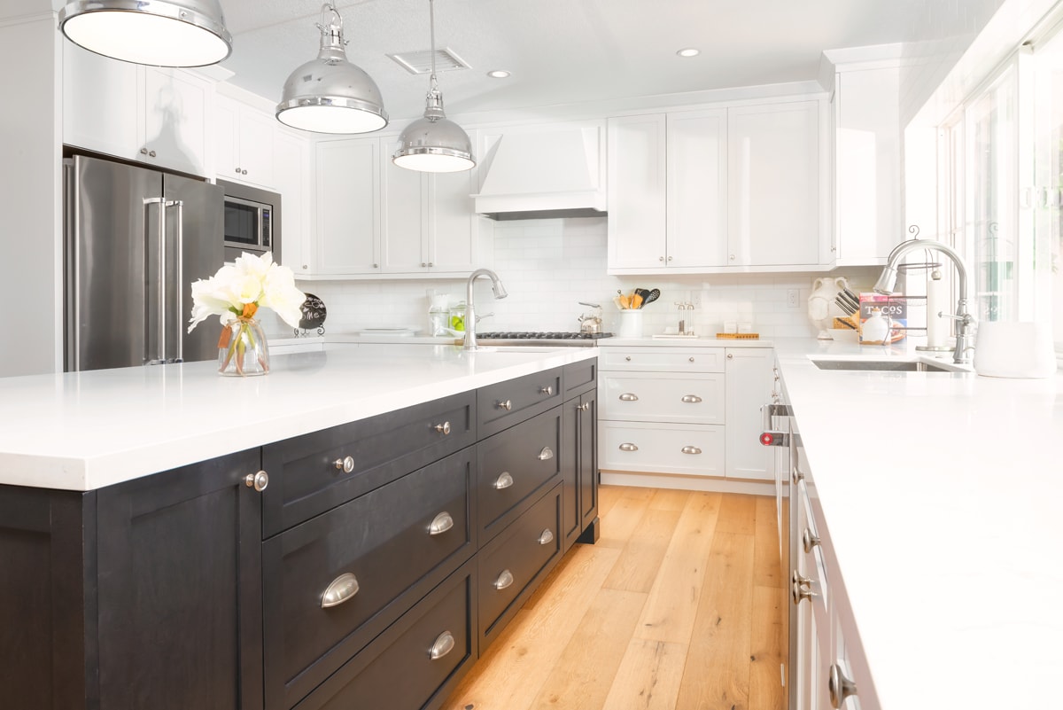 A white kitchen with a dark brown island and silver light fixtures.