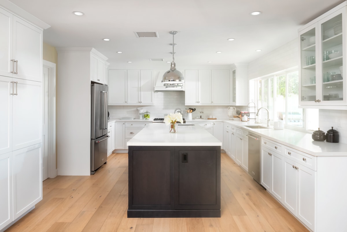 Looking into a kitchen with floor to ceiling white cabinetry with a dark brown kitchen island.