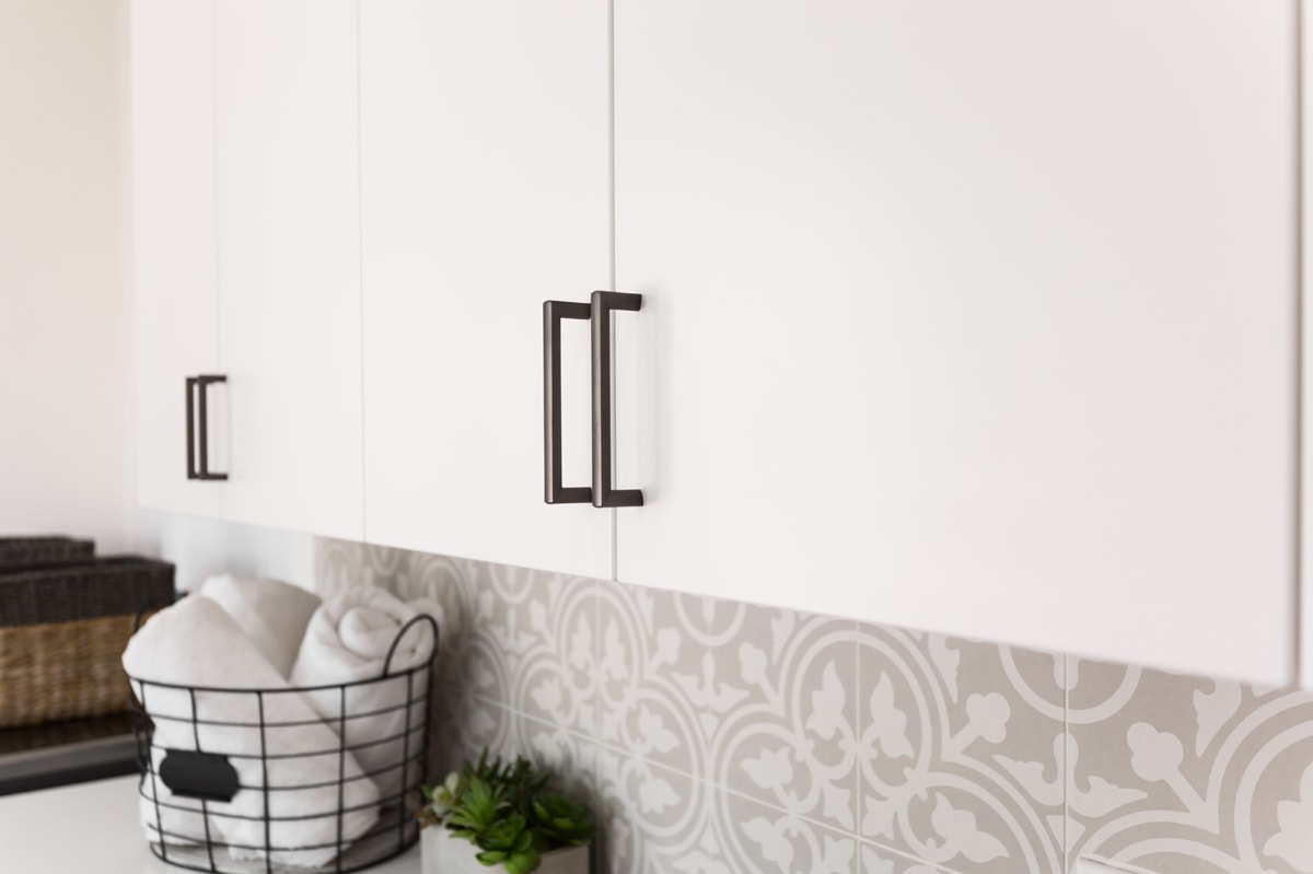 Close-up photo of white cabinets with black hardware and a detailed white and beige tile backsplash.
