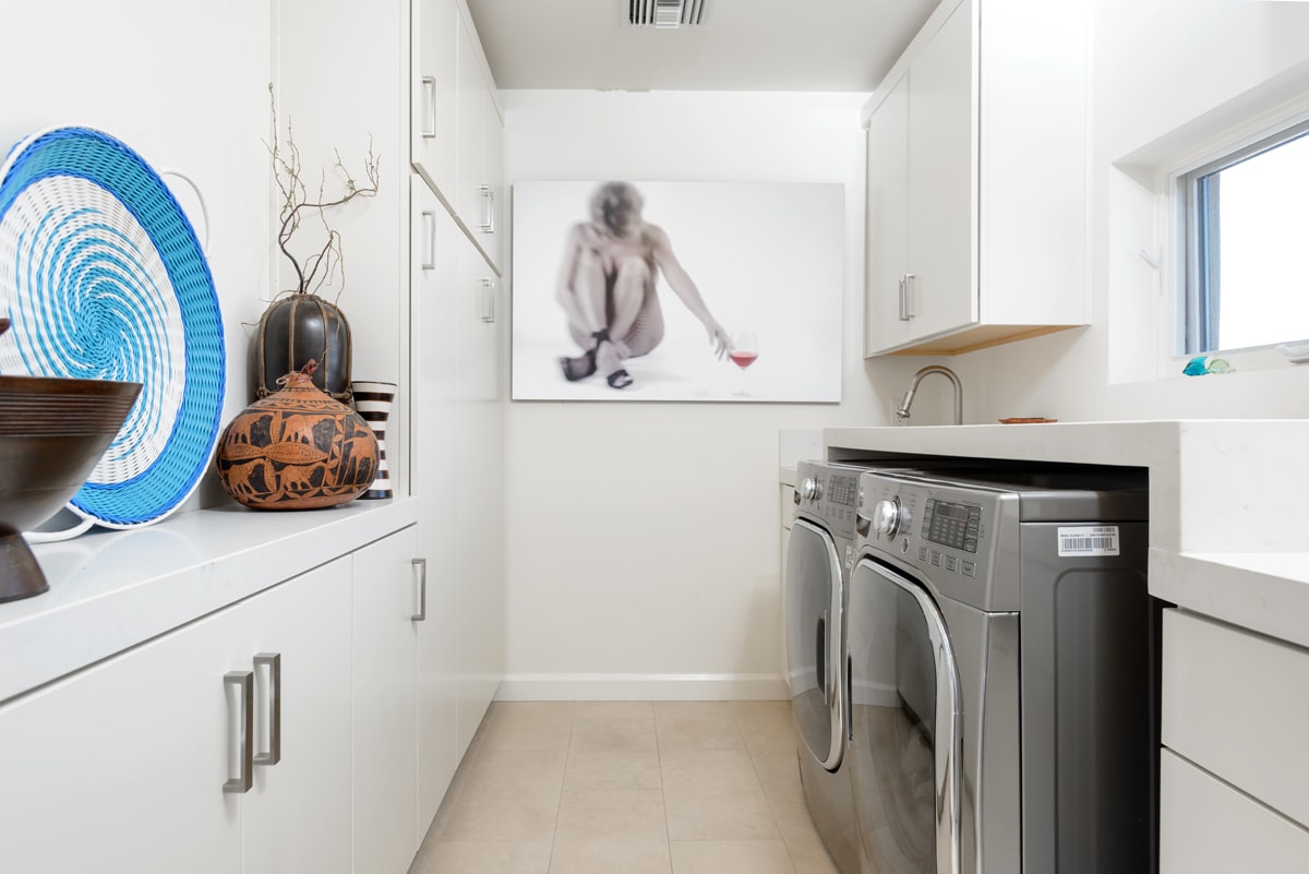 Narrow laundry room with a washer and dryer on one side and floor-to-ceiling white cabinetry on the other side.